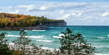 Image of colorful trees on peninsula jutting into blue ocean with blue skies