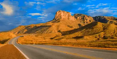 Image of winding road through desert with cliffs and blue sky