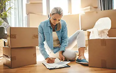 Image of woman completing paperwork on the floor surrounded by moving boxes