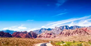 Image of desert with highway in foreground and mountains below a beautiful blue sky