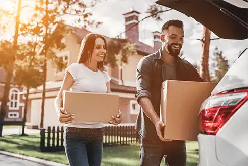 Image of a smiling man and woman carrying boxes to a car