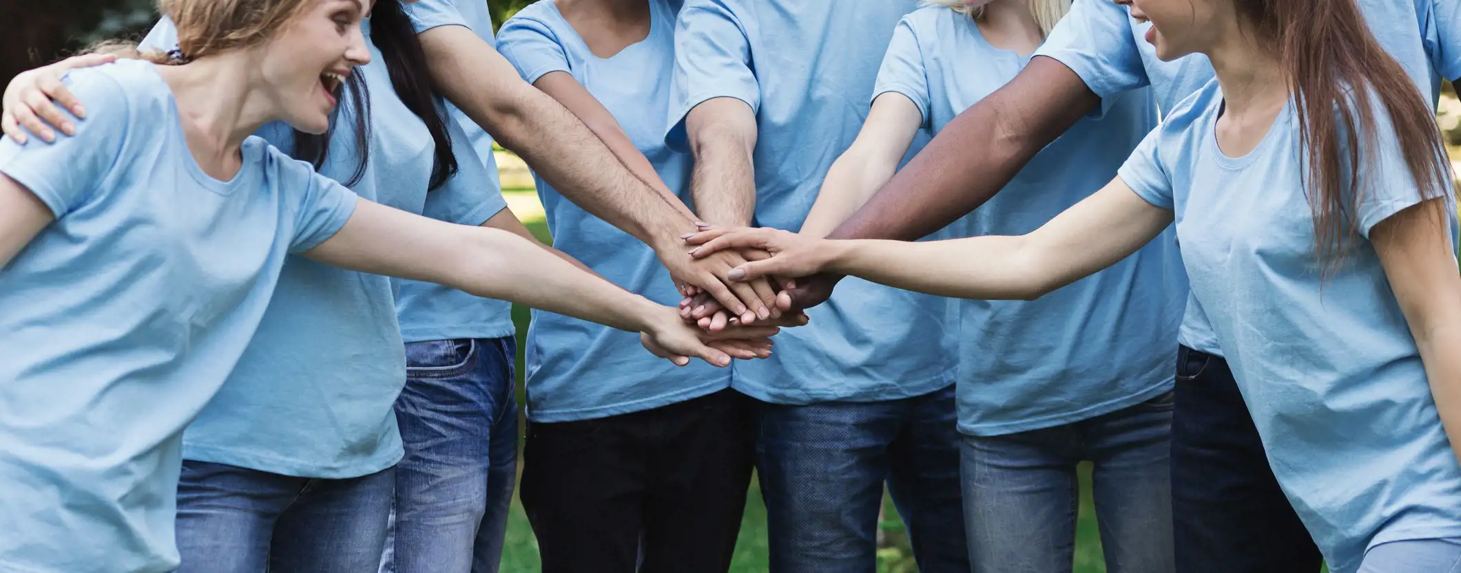 Image of people grouped together stacking their hands in support of giving back to the community