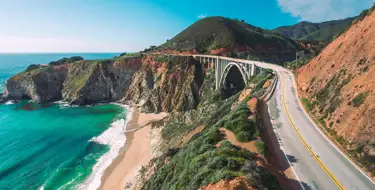 Image of winding road along the ocean with mountains in distance